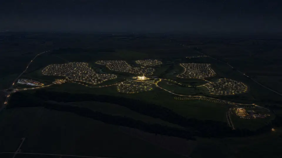 Vista aérea noturna com o desenho do viário e das quadras revelado pela iluminação sobre o terreno escuro